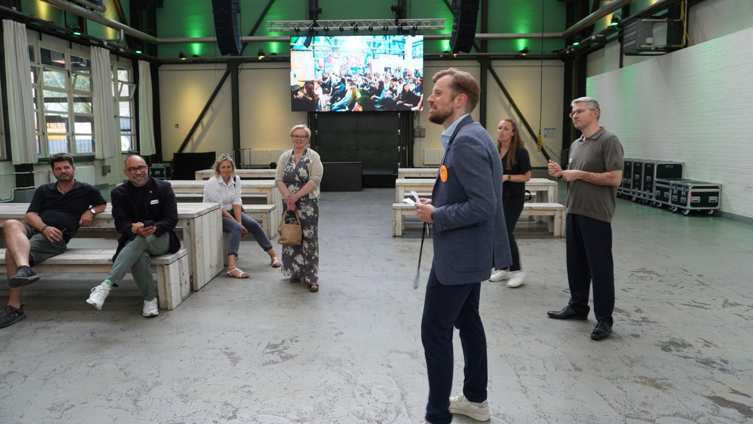 Eine kleine Menschengruppe besucht mit einem Teammitglied der EUREF Event die Location Werkstatt, sie stehen in einem der Räume und hören zu.
