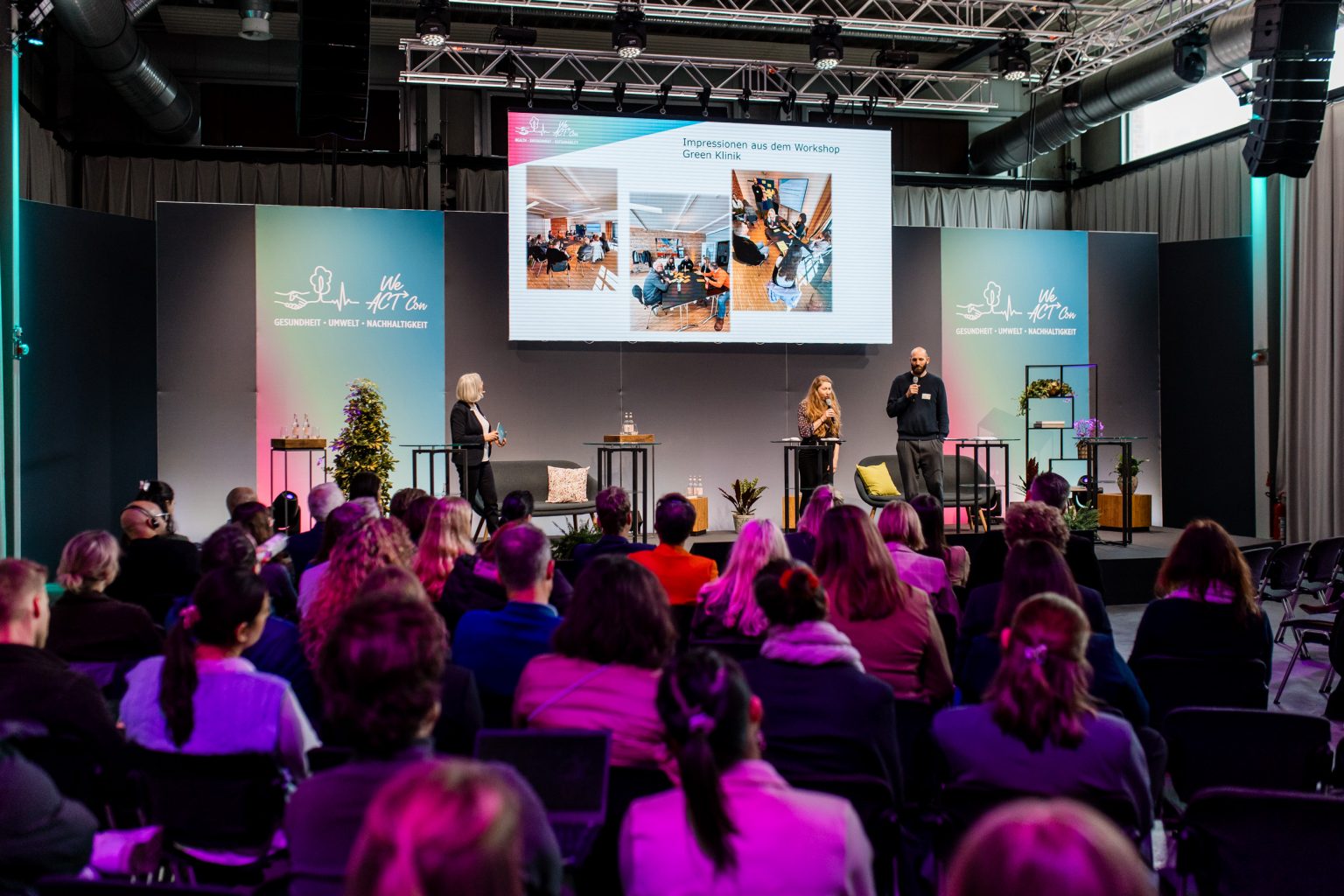 Ein Vortrag in der W26, Bühne mit 3 Rednern, die etwas präsentieren, eine Leinwand mit einer Präsentation