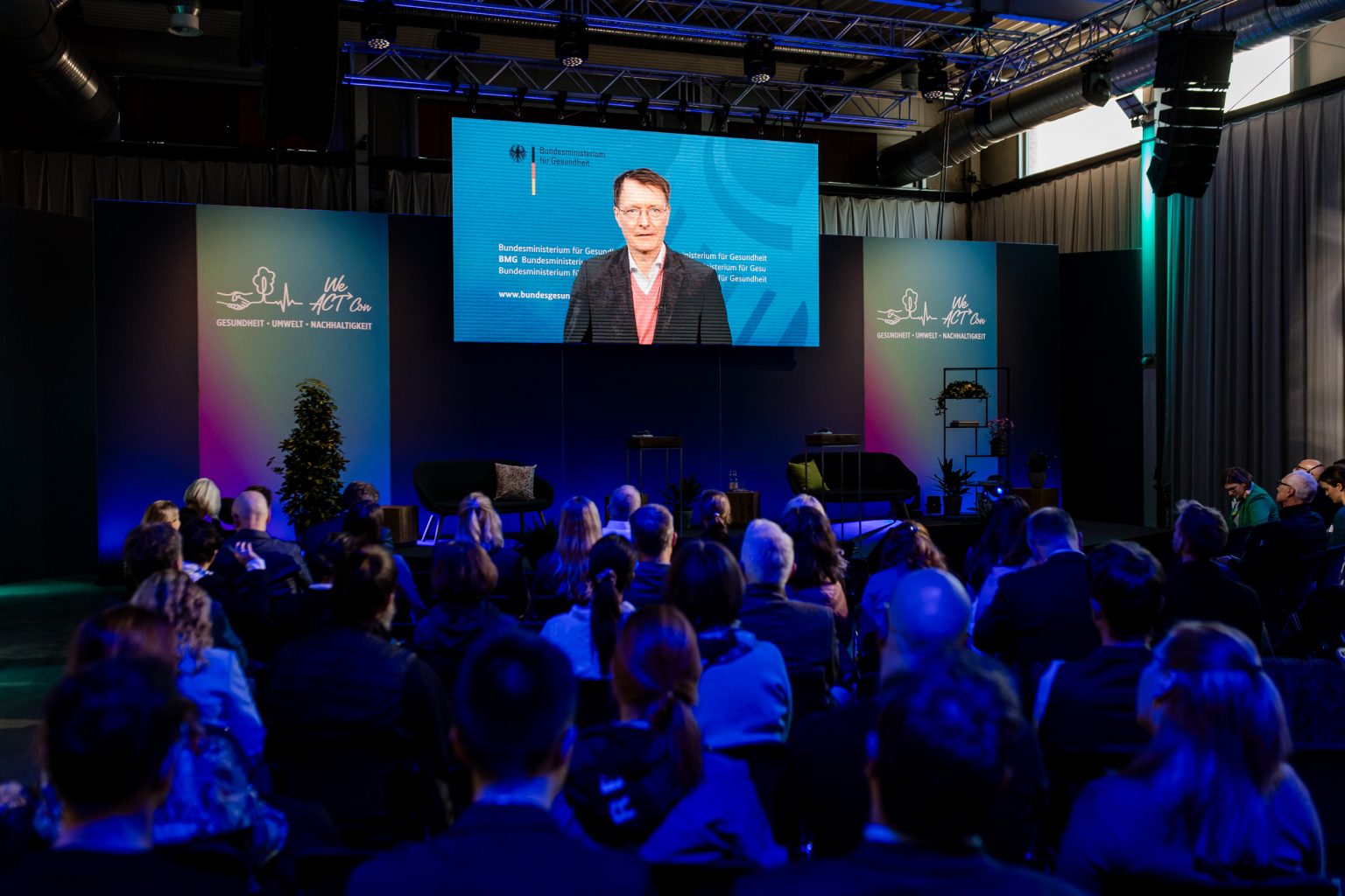 Minister Karl Lauterbach ist auf einer Leinwand zu sehen, eine Botschaft wird von ihm für das Publikum abgespielt