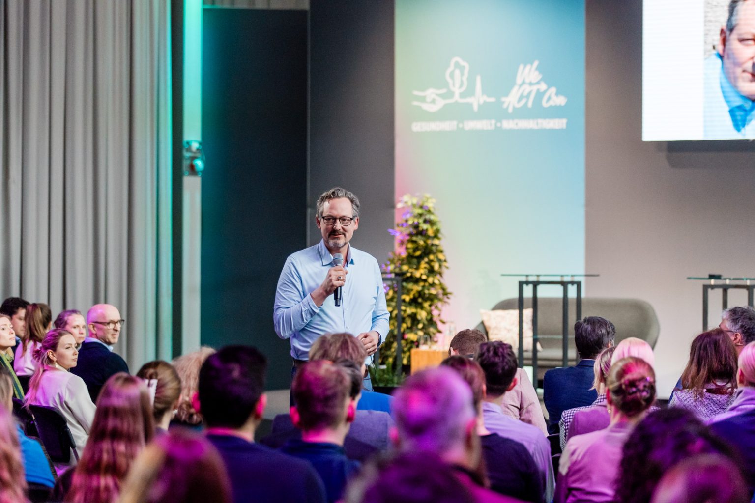 Eckard von Hirschhausen spricht mit Mikrofon vor Gästen auf einer Bühne