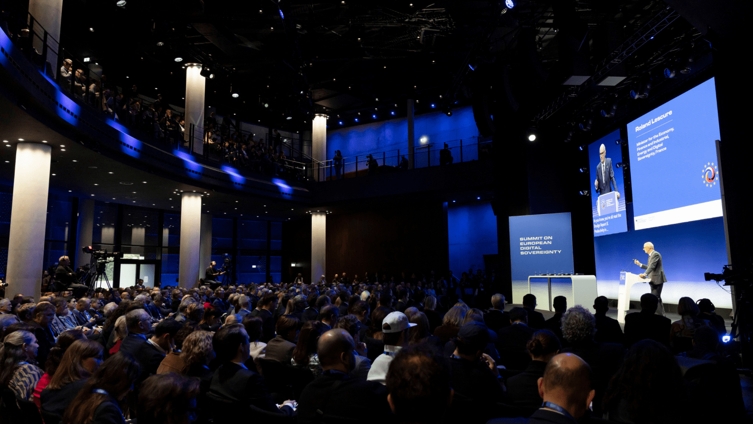 Blick in das vollbesetzte Forum des Gasometers. Auf der Bühne spricht Roland Lescure, französischer Minister für Wirtschaft