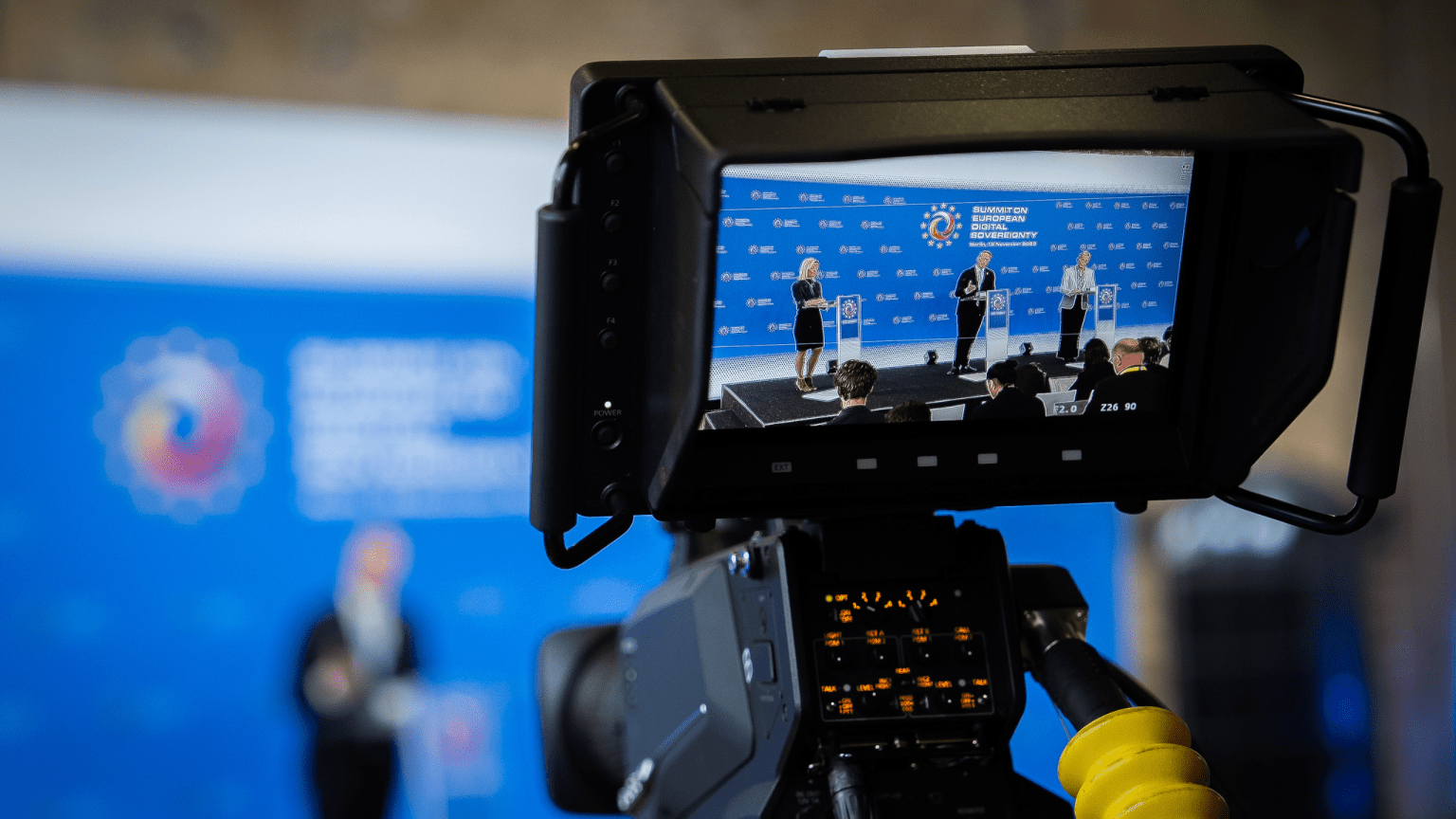 Eine Kamera filmt die Pressekonferenz im Audimax. Auf der Bühne sind leicht im Hintergrund die Redner zu sehen.