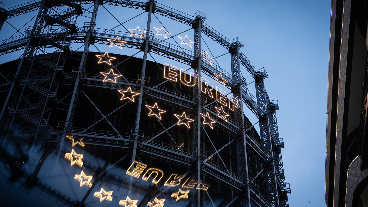 Der leuchtende EUREF-Schriftzug mit dem Sternenkranz am Gasometer bei Abendstimmung