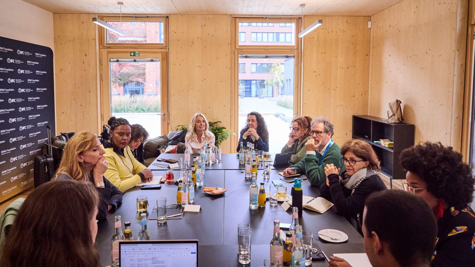 Ein Workshop im Holzhaus: Eine Gruppe von Menschen sitzt an einem eckigen Tisch und diskutiert