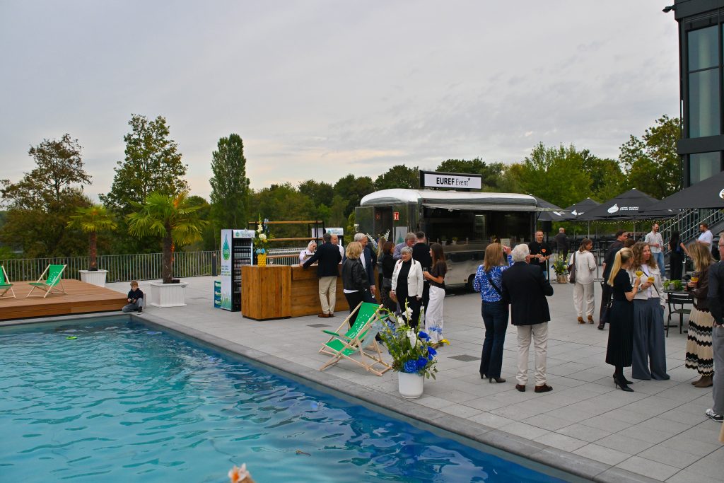 Pool und Beckenrand mit Menschen, die sich unterhalten.