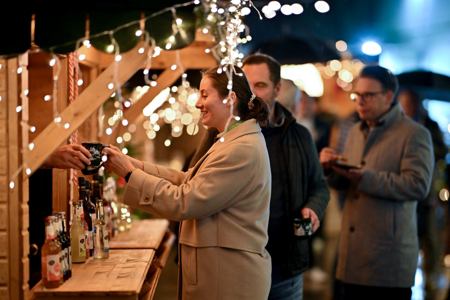 Ein Gast greift nach einem Glühwein, der ihr aus einer der Hütten gereicht wird.