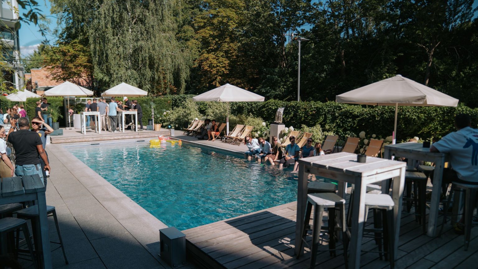 Der Blick geht auf den Pool, am rechten Rand sitzen Gäste mit beinen im Wasser