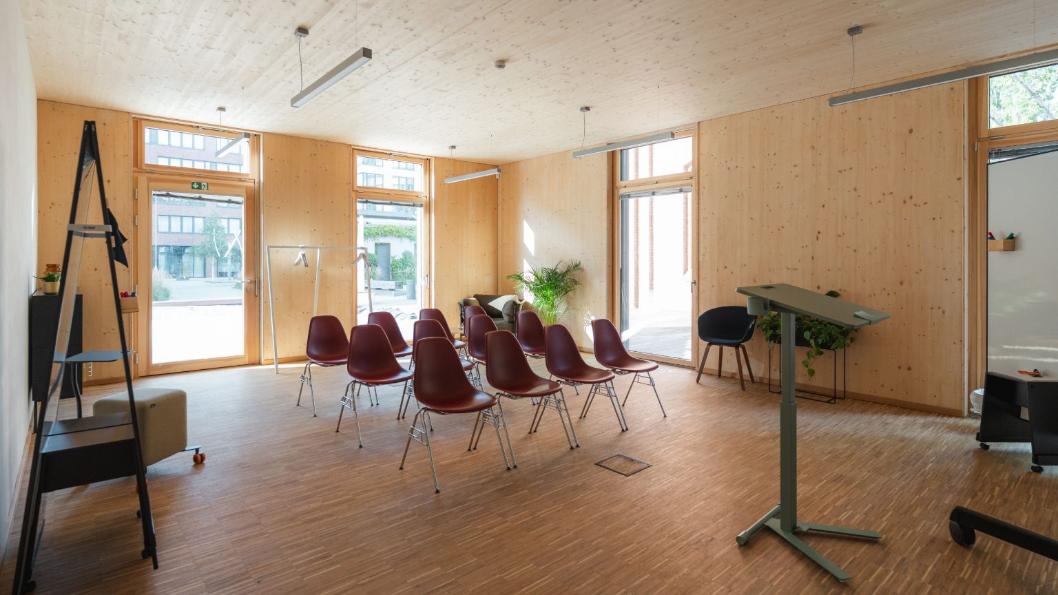 Blick in den Breakout 3 im Holzhaus, das Licht scheint durch die Fenster, rote Stühle stehen in Reihe