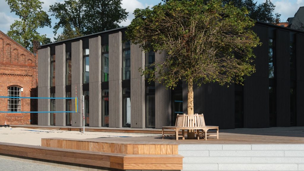 Außenansicht des Holzhauses mit einer Sitzbank im Vordergrund und dem Beachvolleyballfeld