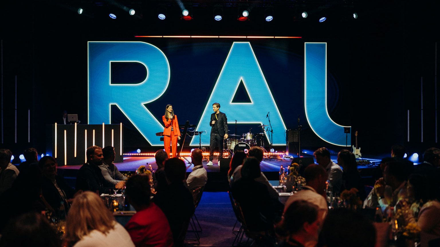 Die Bühne bei der Abendveranstaltung der MOMENTUM, zwei Moderatoren auf der Bühne, große Letter im Hintergrund