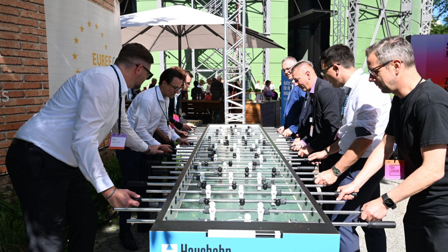 An einem übergroßen Kickertisch spielen Gäste Tischkicker, die Stimmung ist locker