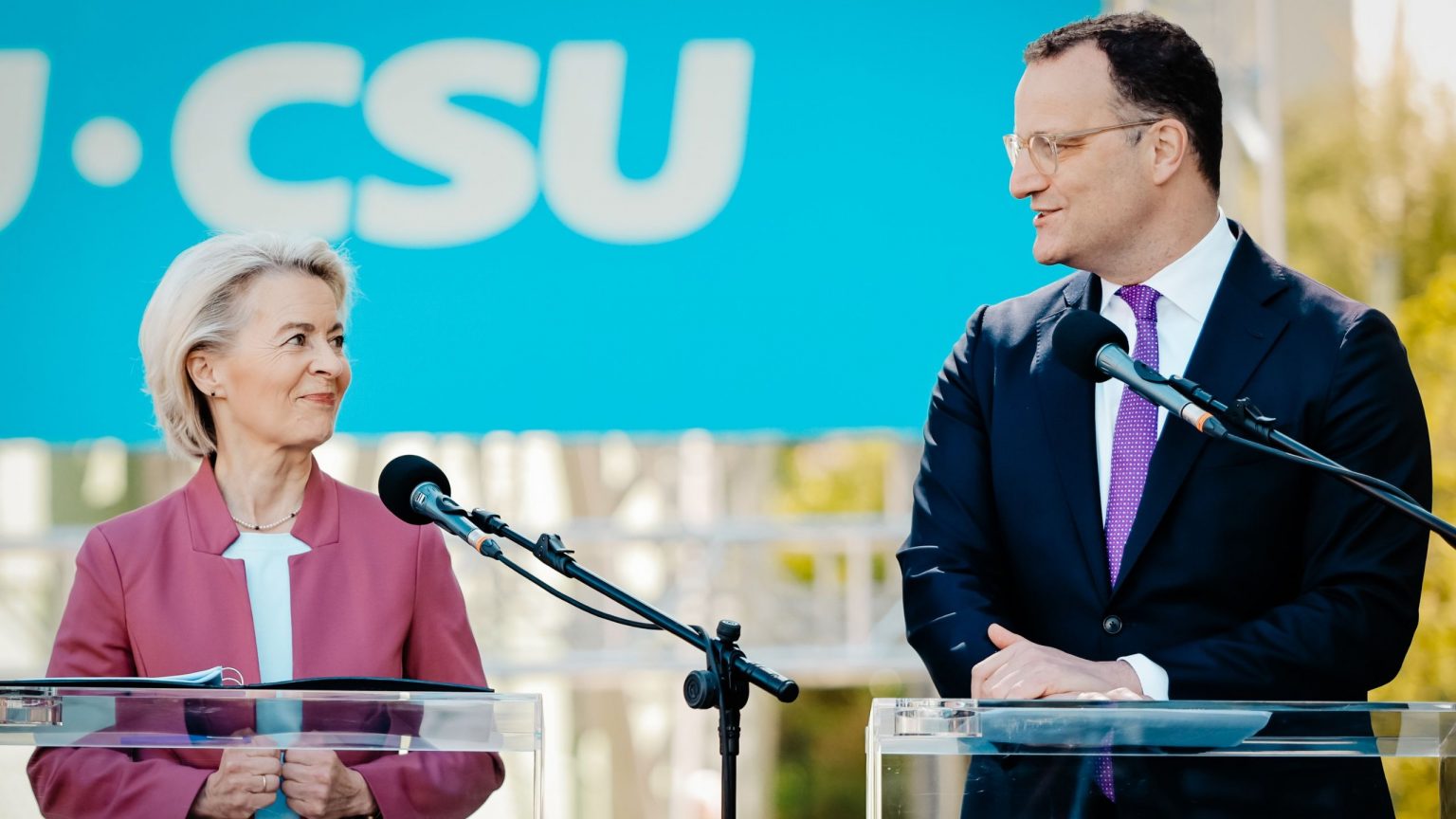 Ursula von der Leyen und Jens Spahn stehen an einem Rednerpult und lachen sich an.