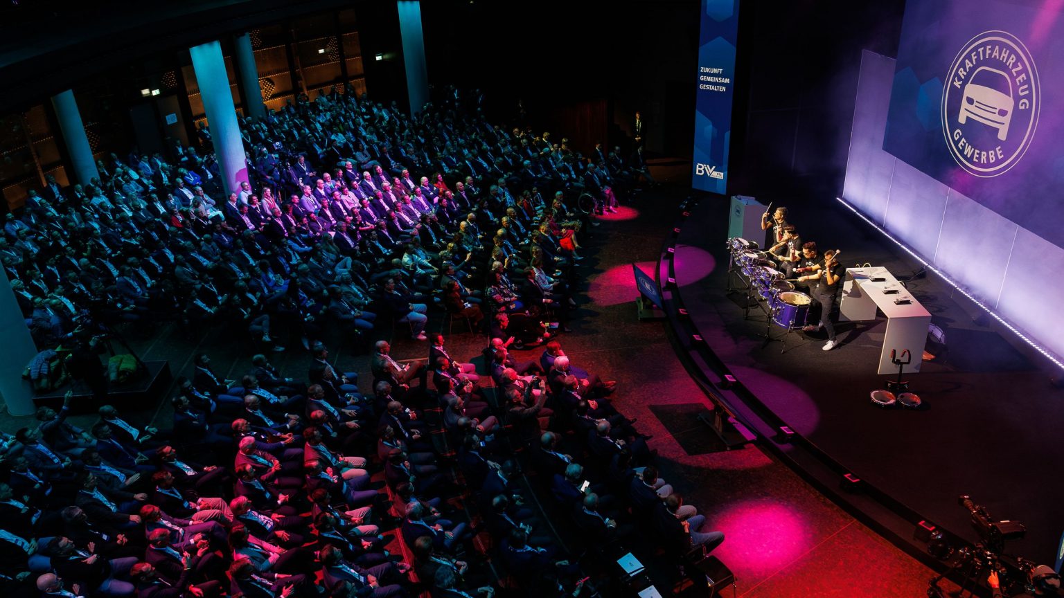 Blick ins FORUM Des Gasometers: 1000 Gäste haben Platz genommen und schauen auf die Bühne, das Licht taucht den Raum stimmungsvoll in pink und blau.