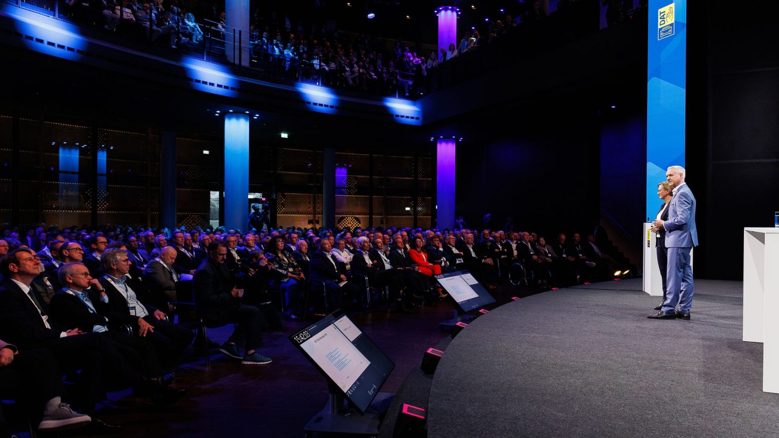 Zwei Moderatoren stehen auf der Bühne im Gasometer und sprechen zum Publikum