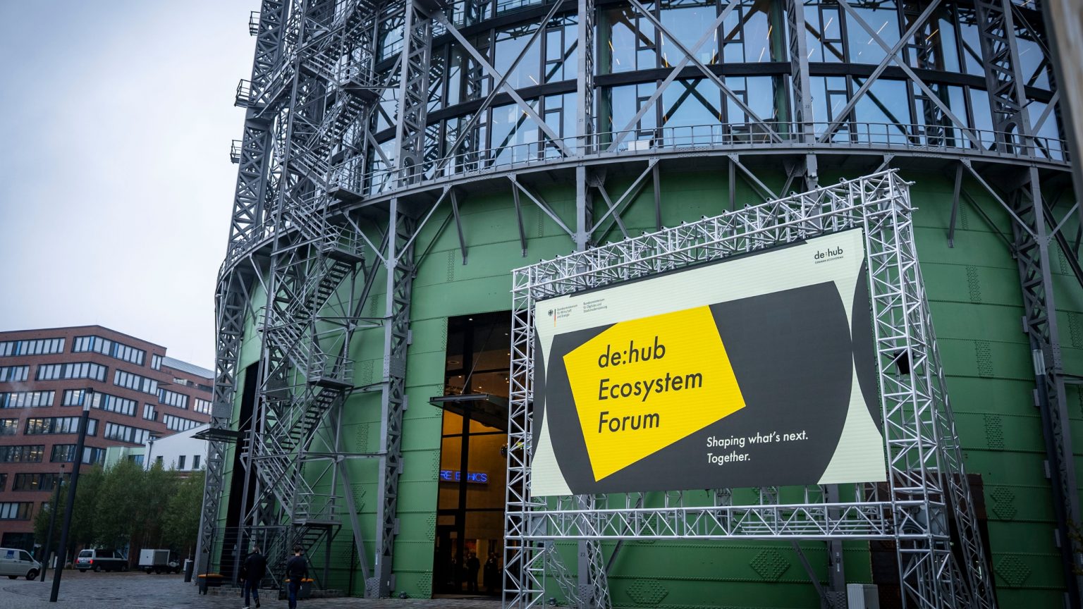 Eine Außenansicht des Gasometers mit dem Veranstaltungsvisual von der Veranstaltung de:hub Ecosystem Forum auf einer LED-Wand.