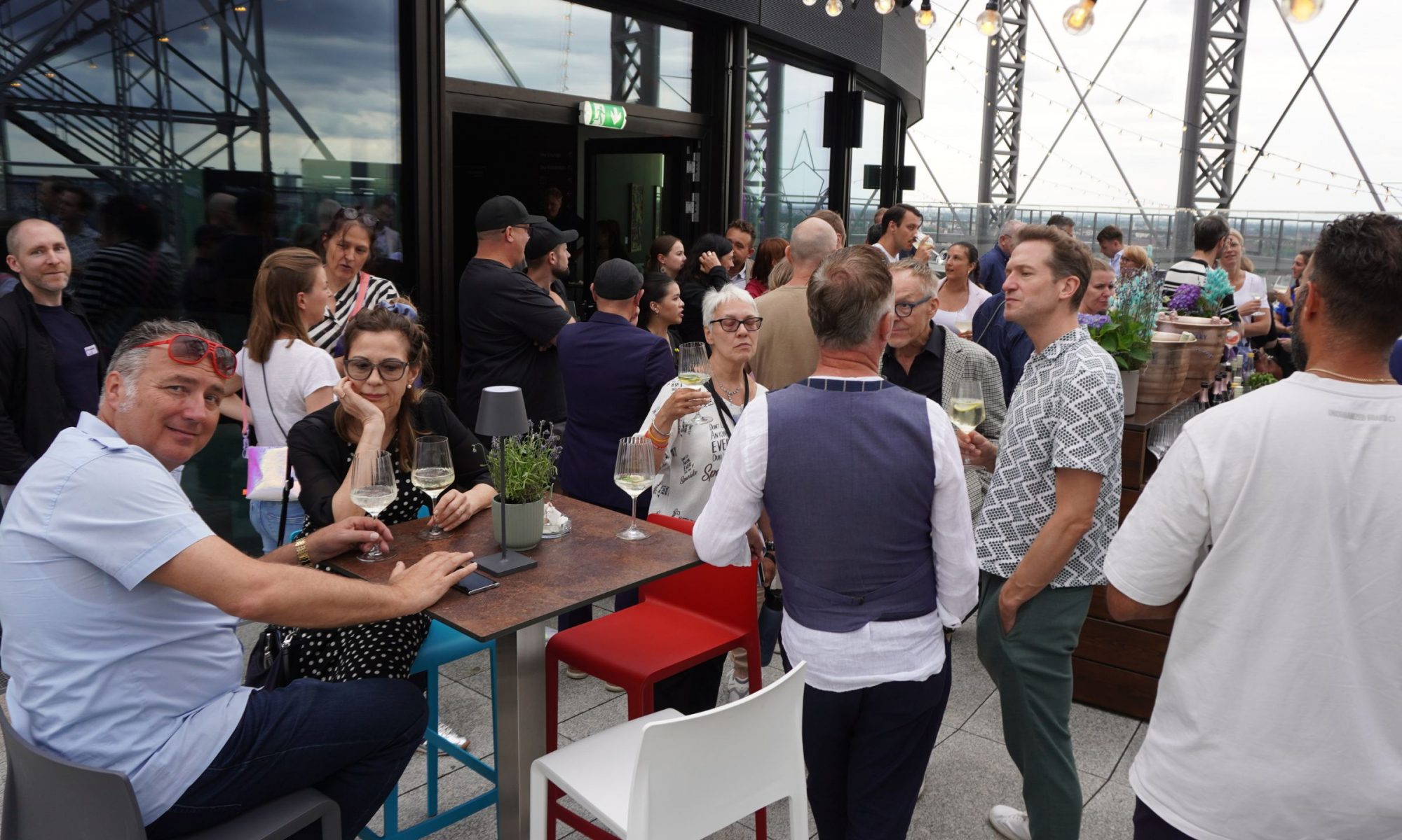 Gäste stehen und sitzen auf der Terrasse des Gasometers und unterhalten sich angeregt